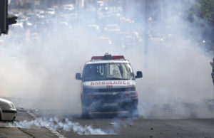 A Palestinian ambulance emerges from a cloud of tear gas.