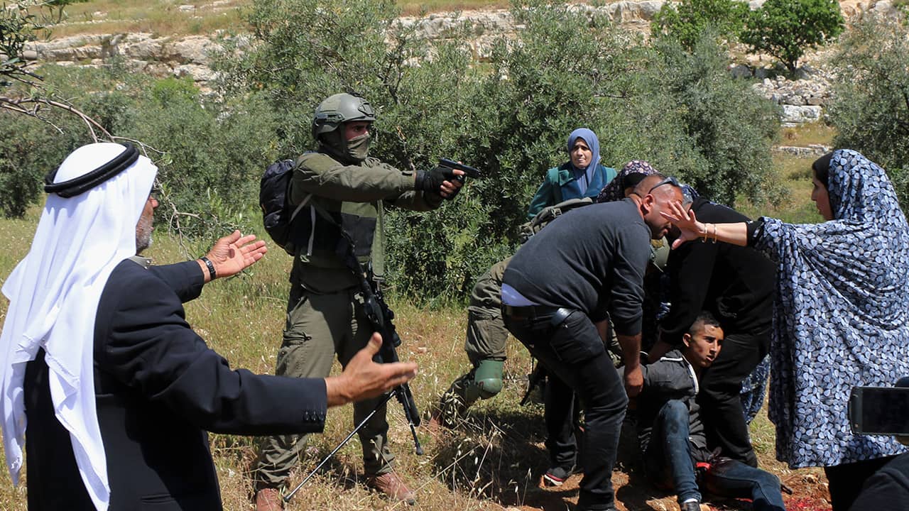 Photo of an Israeli soldier pointing his pistol at a group of Palestinians