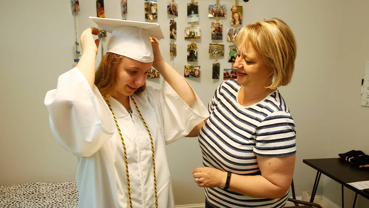 Photo of Emilee Taylor trying on her graduation cap and gown with her mother