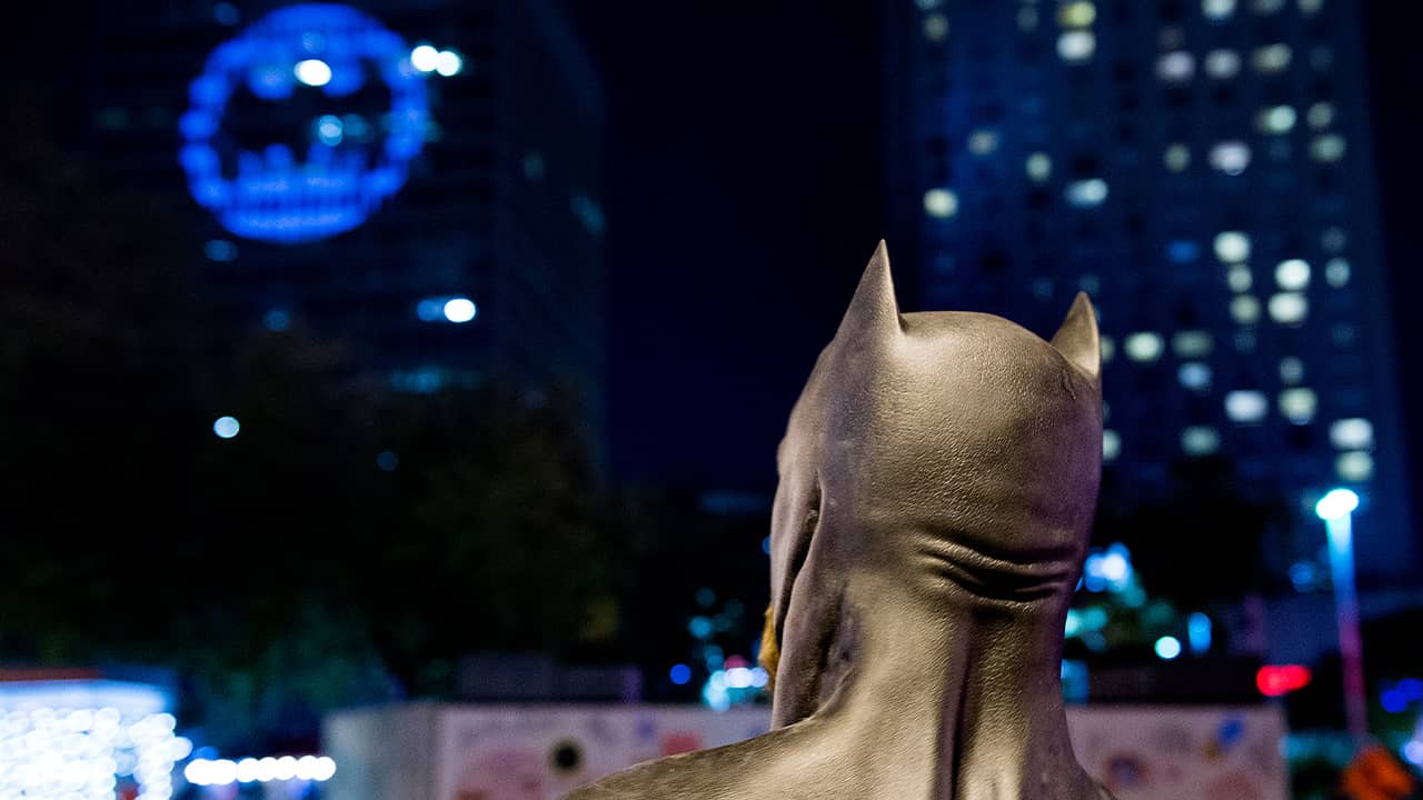 Photo of a man dressed as Batman looking up at a bat signal in Montreal