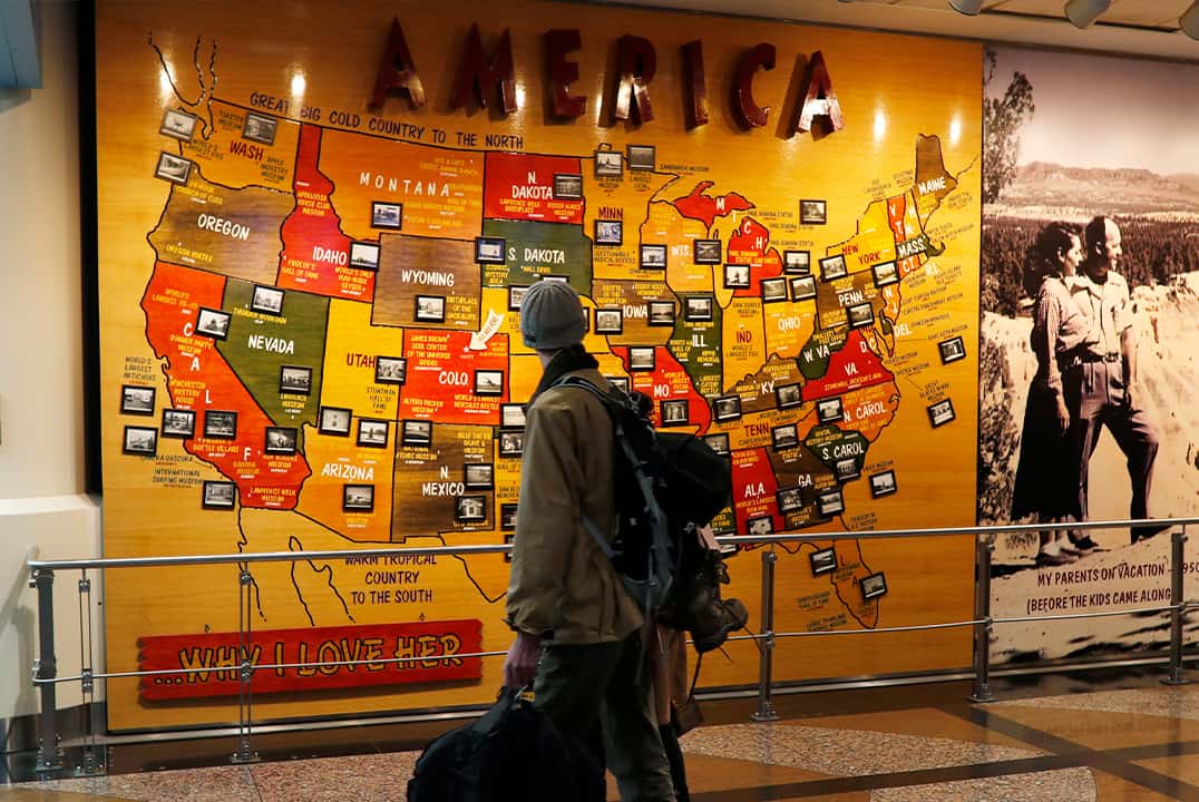 Photo of a traveler passing by a map of the U.S. at the Denver International Airport