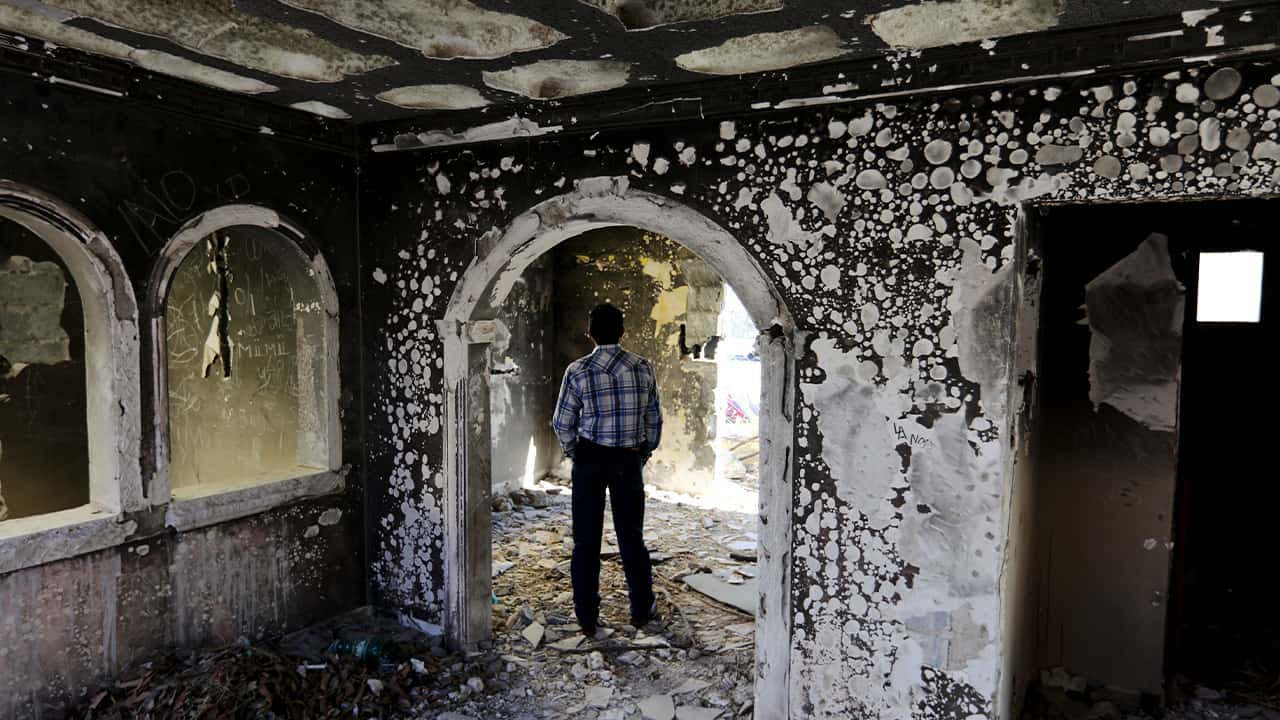 Photo of a former policeman walking through an abandoned home torched by the Zetas cartel