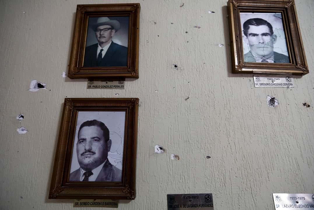 Photo of portraits of former mayors hang on a wall riddled with bullet holes, Mexico