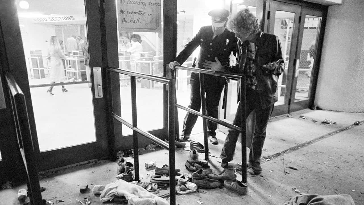 Photo of a security guard and an unidentified man look at an area where several people were killed