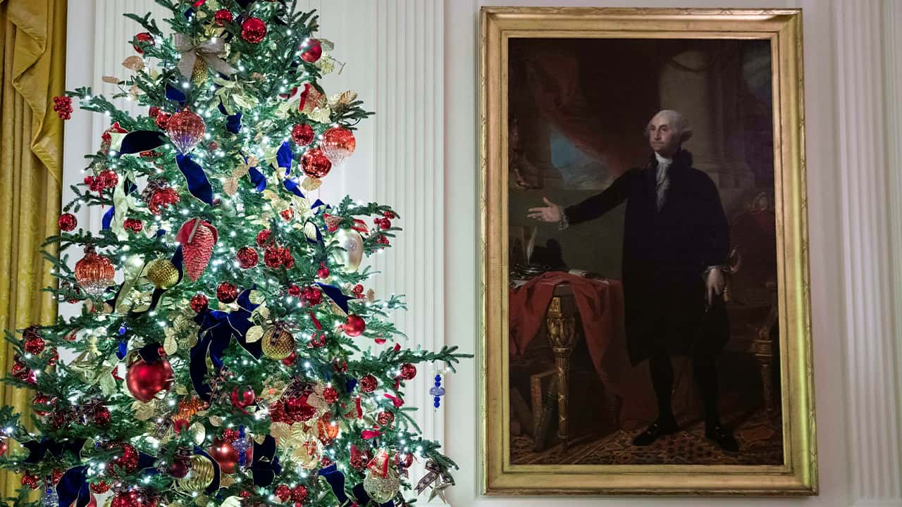 Photo of a decorated tree stands next to the portrait of President George Washington in the East Room