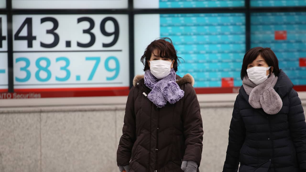 Photo of people walking by an electronic stock board of a securities firm in Tokyo