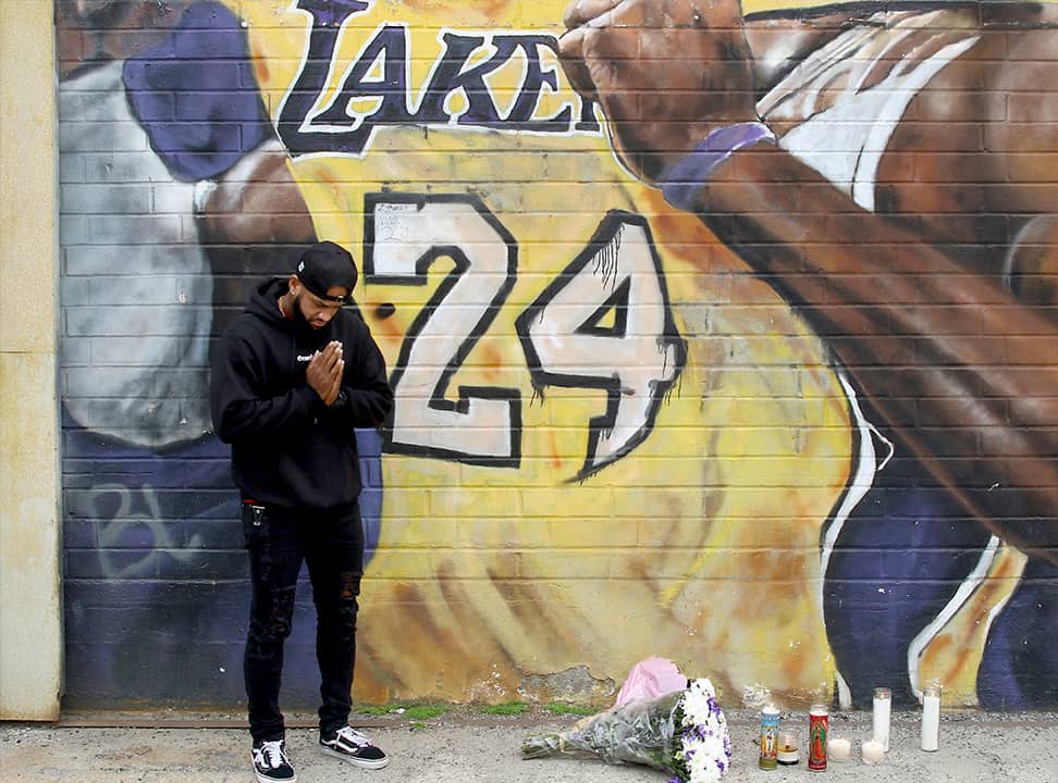 Photo of a man praying at a mural of Kobe Bryant in LA