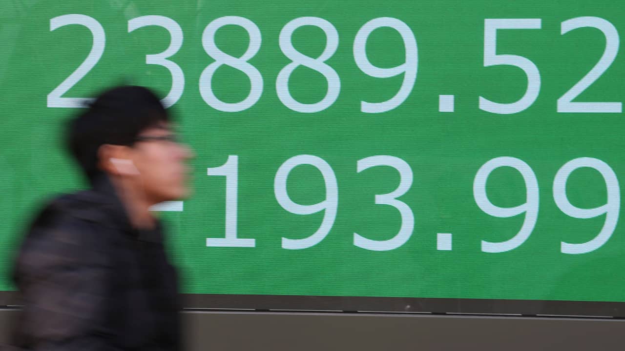 Photo of a man walking by an electronic stock board of a securities firm in Tokyo