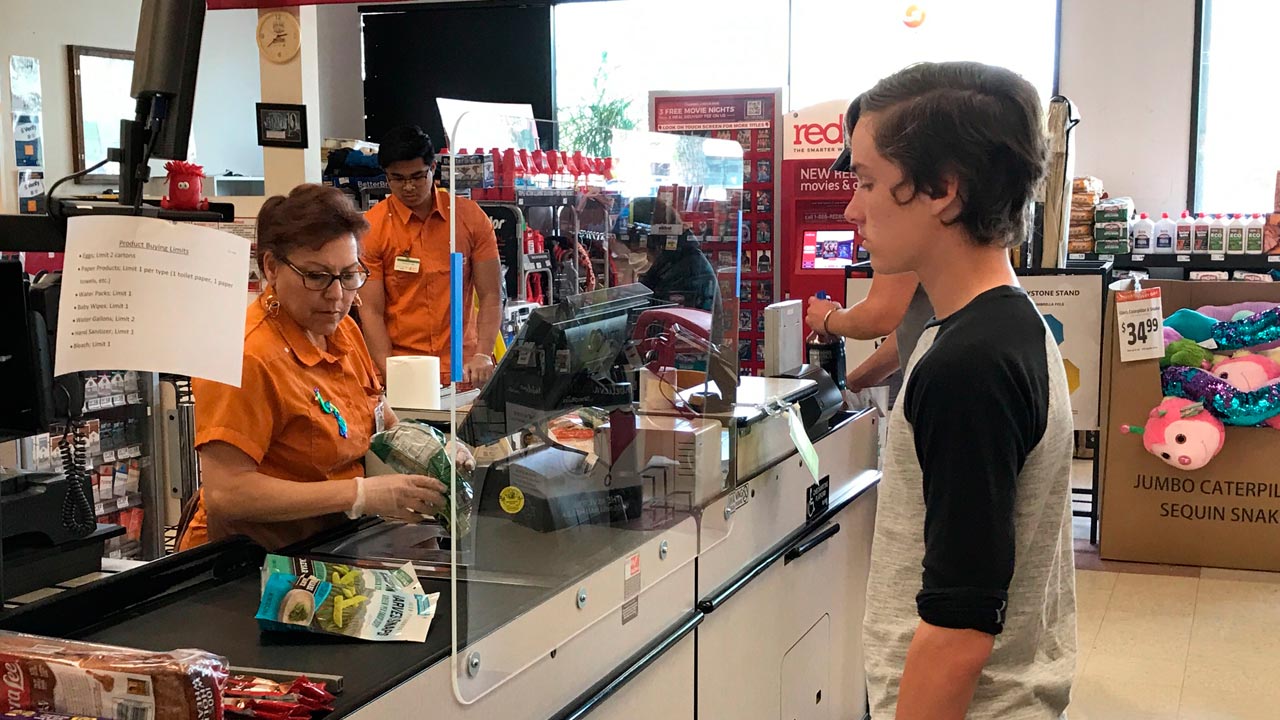 Photo of customer and grocery store cashier separated by a sneeze guard