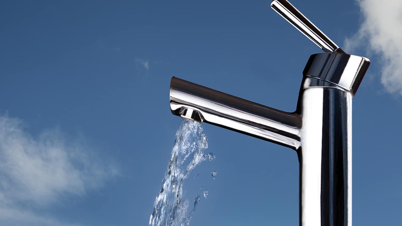 Photo of water coming out of a faucet against a backdrop of blue skies