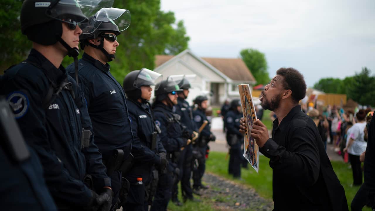 Photo of a man standing in front of a line of cops